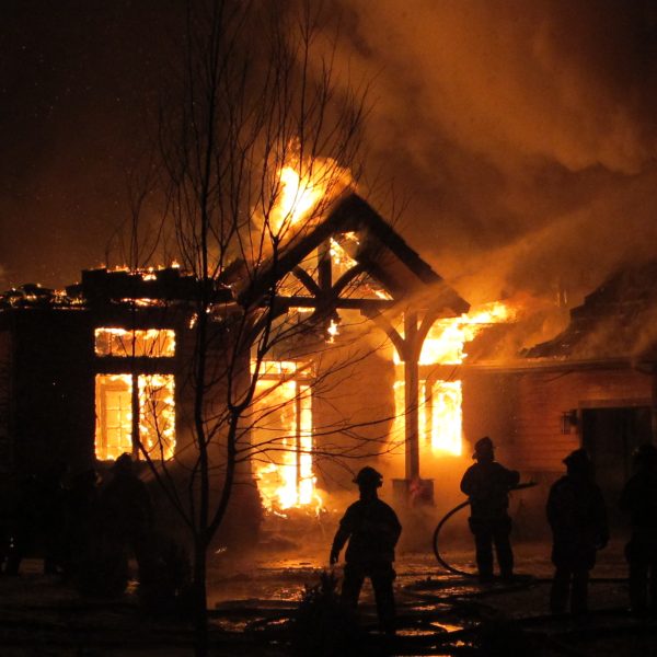Firemen use a fire hose to try and put out a house fire during a snowfall.
