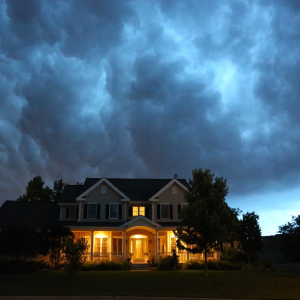 A well appointed house is lit up while a large thunderstorm moves in overhead. Ample copy space above.